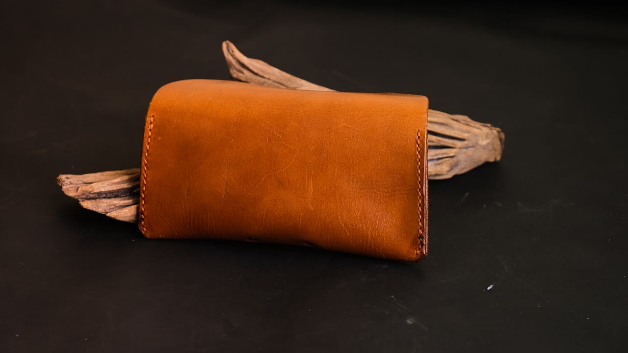 Elegant brown leather wallet displayed on a rustic wooden piece with a black studio backdrop.