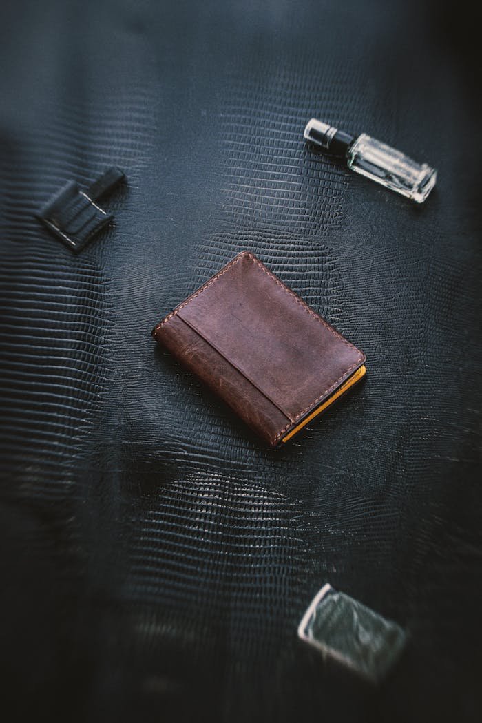 Top view of a stylish leather wallet with accessories on a textured surface.