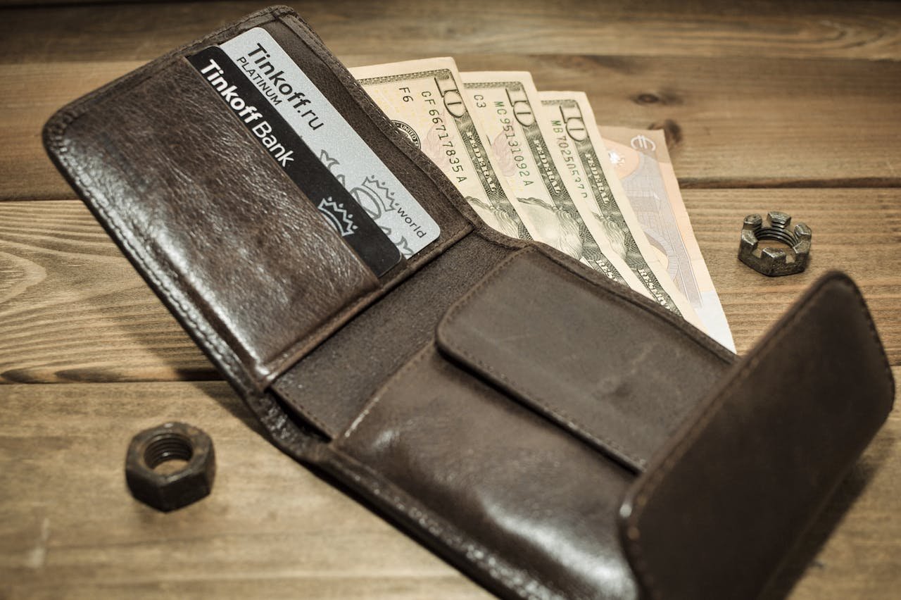 Open leather wallet displaying cash and credit cards on a rustic wooden background.