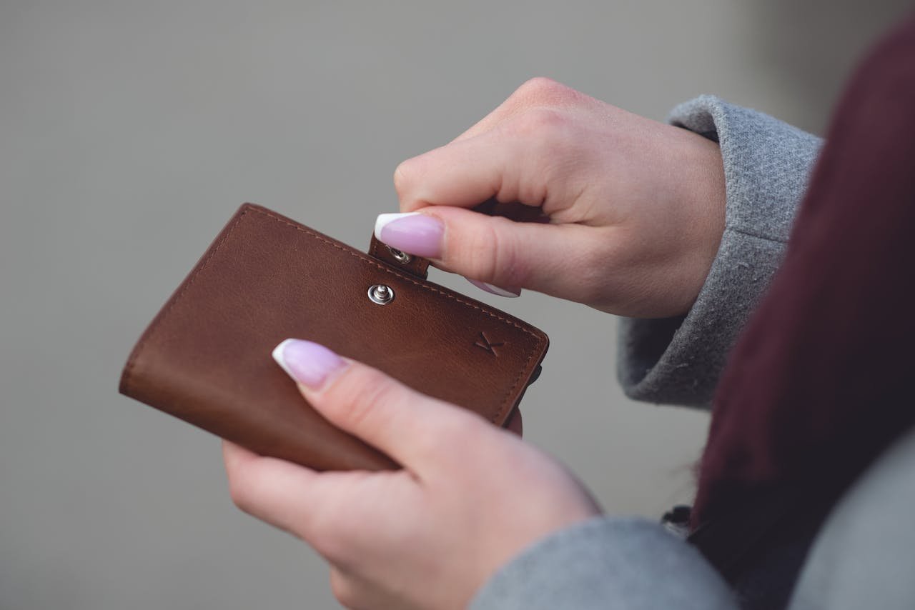 Hands with manicured nails holding a small brown leather wallet, showcasing style and elegance.