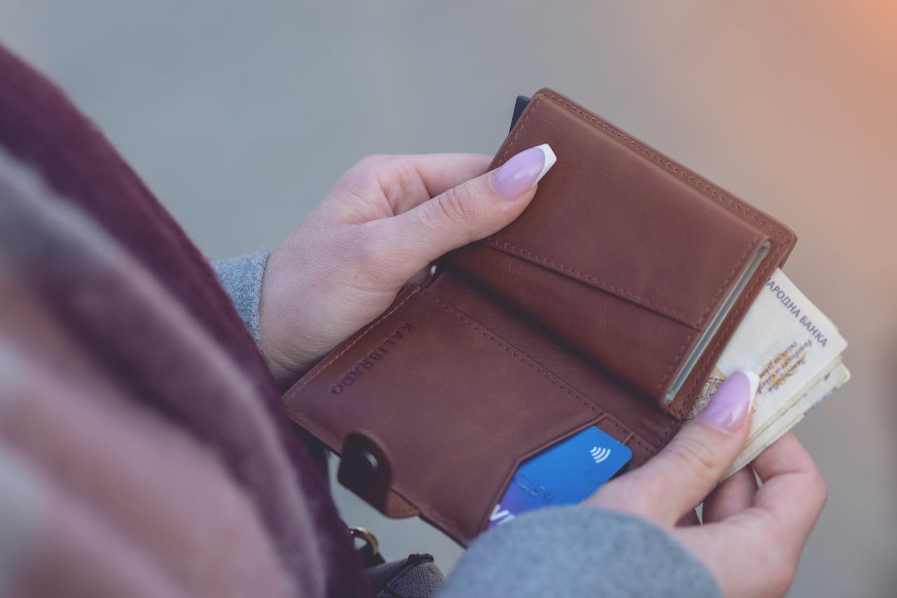 Home Close-up image of hands holding a brown leather wallet with banknotes and a credit card visible.